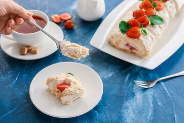 Woman eating delicious meringue roll with strawberry on table