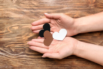 Female hands with paper hearts on wooden background. Racism concept