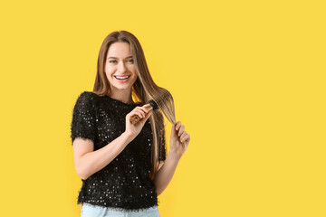 Young woman brushing hair on color background