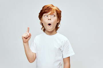 Portrait of a red-haired boy with an open mouth and showing his index finger up Copy space