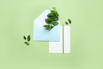 Envelope with paper sheet, pencil and green leaves on color background