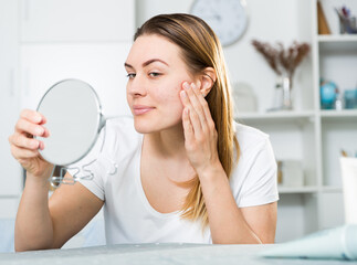 Cheerful woman is concentrared looking on her face in the mirror at the home.