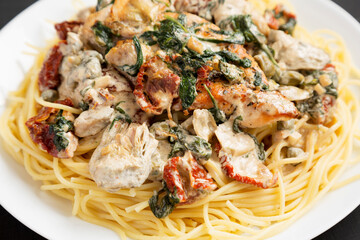 Homemade Creamy Tuscan Chicken with Pasta on a white plate on a black background, side view. Close-up.