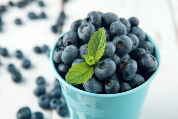 Close-up blue bucket with blueberry and mint leaves on white wooden table.