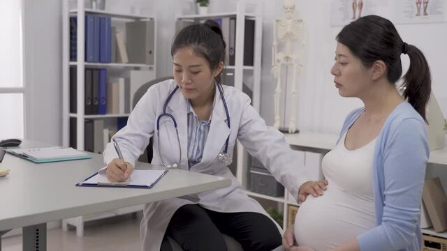 female gynecologist palpating pregnant woman's tummy, and determine the height of the fundus of the uterus and writing on a clipboard.