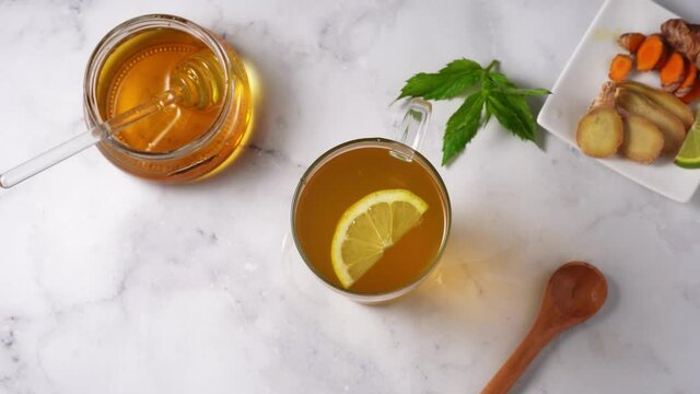 Top view of glass cup with turmeric ginger tea and jar of honey on white background. Lemon rotating in a cup. 4K