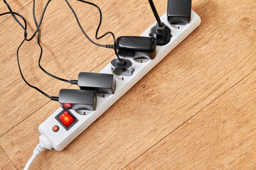 Electrical power strip overloaded with multiple electrical cords plugged in. Many plugs plugged into electric power bar