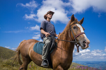 Fototapeta premium A rider in a wide-brimmed cowboy hat on a horse against a blue sky.