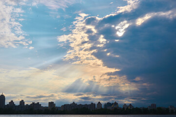 Sun rays breaking through the dark clouds above the river and the city.