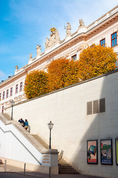 vienna, austria - OCT 17, 2019: back side entrance of albertina museum building. lantern and logo on the stairs. trees in fall foliage. statues on the roof. sunny afternoon
