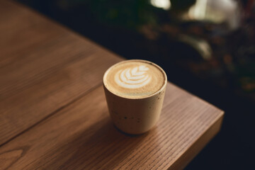 Cup of cappuccino with latte art on the wooden table. Beautiful foam and ceramic cup