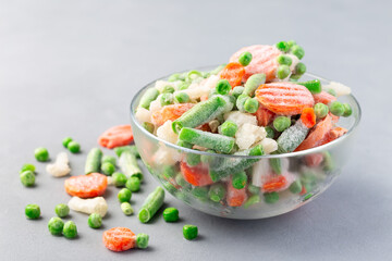 Glass bowl with frozen vegetables on table, green peas, carrot, cauliflower,  green beans,...