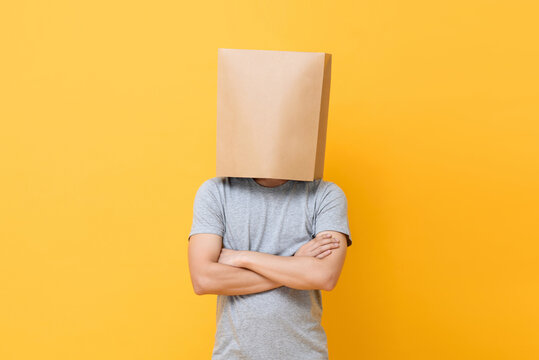 Concept portrait of Anonymous man with head covered with paper bag doing arms crossed gesture in yellow studio background