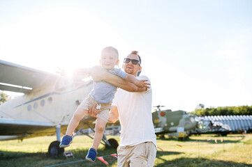A dad and toddler spend time outdoors in an airplanes museum. A young father carries baby boy in hands like a airplane, they have fun together. © Vadim Pastuh