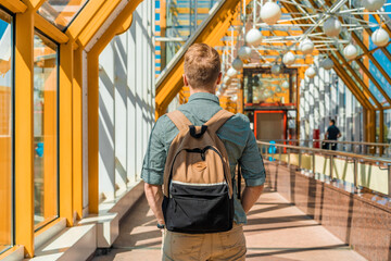 Fototapeta na wymiar A young man with a backpack walks on a futuristic yellow pedestrian bridge in Moscow