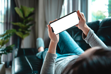 Woman using mobile smartphone with blank white screen on a sofa in living room, copy space.