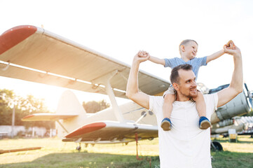 Family time. A dad and cute son spend time in park of retro airplanes. A daddy carries toddler on his shoulders, they are holding hands © Vadim Pastuh