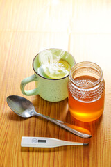 Infusion based on lemon and ginger, with honey, accompanied by a thermometer on a wooden table. Home remedies to relieve symptoms of the flu, cold or COVI-19