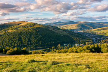 Fototapeta premium rural landscape in mountains at sunset. grassy pasture on the hill in evening light. high mountains in the distance. beautiful clouds on the blue sky. wonderful early autumn scenery