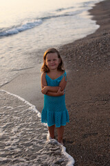 child a girl in a blue knitted dress by the sea walks and watches the sunset. Turkey