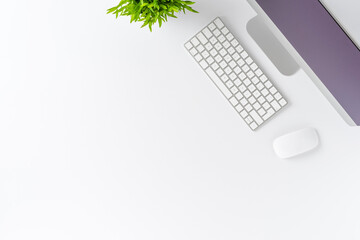 Modern computer with accessories and small flower on white background with copyspace. Top view