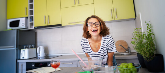 Beautiful happy young woman preparing dessert at home in the kitchen laughing joyfully, hobbies and...