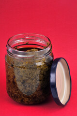 Pot de sauce au pesto ouvert en gros plan sur fond rouge