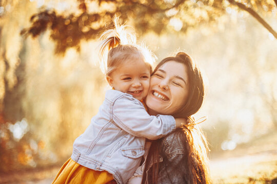 young happy and smiling mom with her little daughter in arms hugging and kissing spending a weekend on a walk in autumn park. selective focus, noise effect,