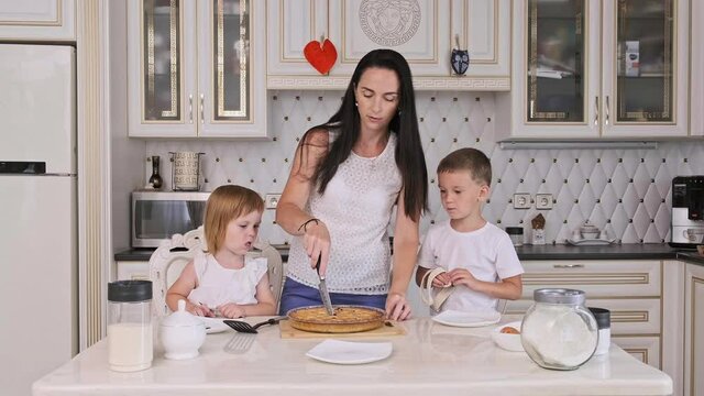Happy family of mother and two kids cutting raspberry pie in kitchen. Pretty mother with little son and daughter at home. 4K, UHD