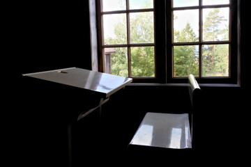 Antique white school bench in a dark classroom lit by ambient sunlight from a window.