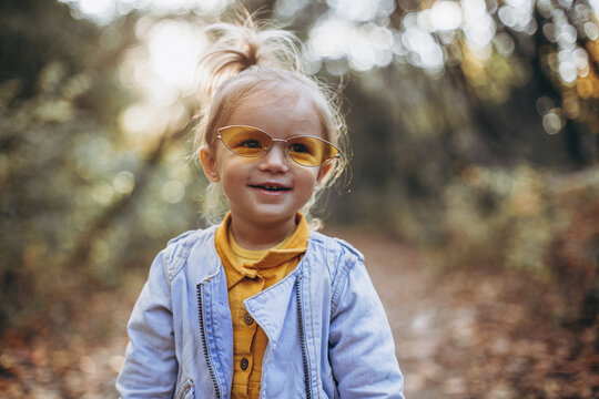 little pretty girl posing for a photo while walking with her parents in autumn park, an infinitely happy and joyful child, selective focus, noise effect