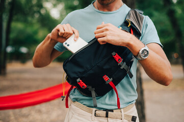 Close photo of a waist bag for advertising. A man in casual clothes puts a white smartphone in the...