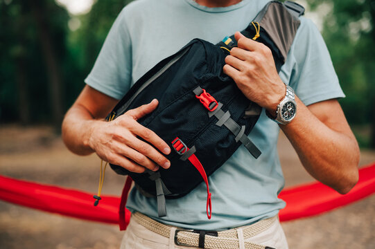 Close up cropped photo of a waist bag for travel on the shoulder of a young man in the woods. Equipment for tourism.