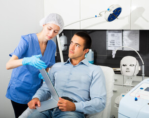 Skilled woman beautician examining face skin of young male patient before cosmetology procedure in beauty clinic