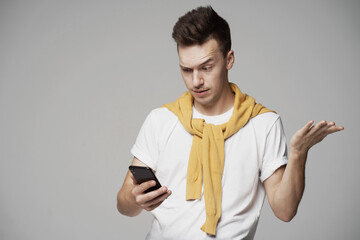 surprised male young student, looking into the phone reads a message from a friend. yellow sweater and white t-shirt. fashionable barbershop hairstyle