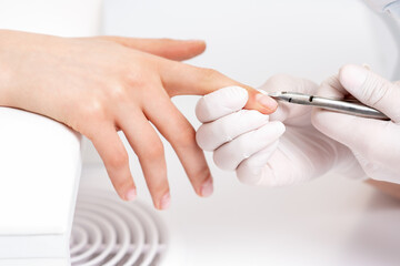 Obraz na płótnie Canvas Close up of manicurist using manicure cutter to remove cuticle of female nails in manicure salon