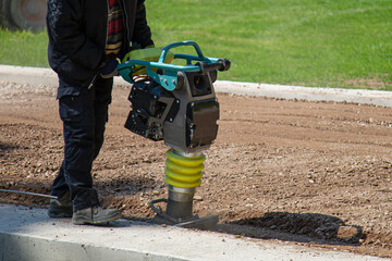 A sandy ground gets rammed with a vibration rammer