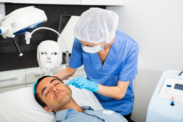 Female cosmetologist injecting carbon dioxide under face skin of male client to increase blood flow...