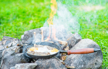 Frying pan with fried eggs and bacon is on the fire in nature