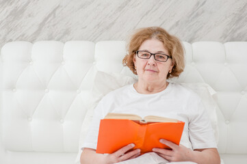 Smiling  senior woman with  book on the bed. Empty space for text