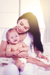 Beautiful mother hugging her baby on bedroom