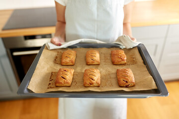 food cooking, culinary and people concept - young woman with towel holding hot baking tray with jam pies at home kitchen