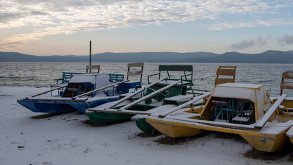 Landscape of a winter lake with multi-colored catamarans in a frozen lake and mountains