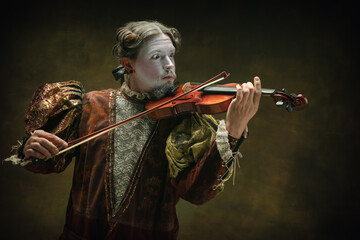 Playing violin. Young man as Johann Bach isolated on dark green background. Retro style, comparison of eras concept. Beautiful male model like historical character, great music composer, old-fashioned