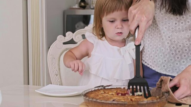 Pretty mother with little son and daughter cutting raspberry pie in kitchen. Happy family of mother and two kids together. Close-up in 4K, UHD