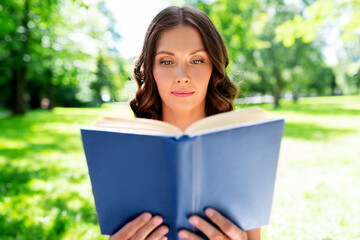 Obraz premium leisure and people concept - beautiful young woman reading book at summer park