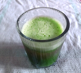 Glass of green vegetable smoothie. bitter gourd and cucumber smoothie glass on the cotton cloth background perspective view