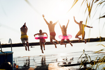 Group of young friends having fun enjoying a summer day swimming and jumping at the lake.