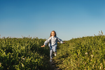 Fototapeta premium Happy girl run in field. Blue sky, green meadow. Girl lose two baby teeth.