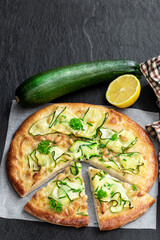 Vegetarian pizza with zucchini and pine nuts on black stone background